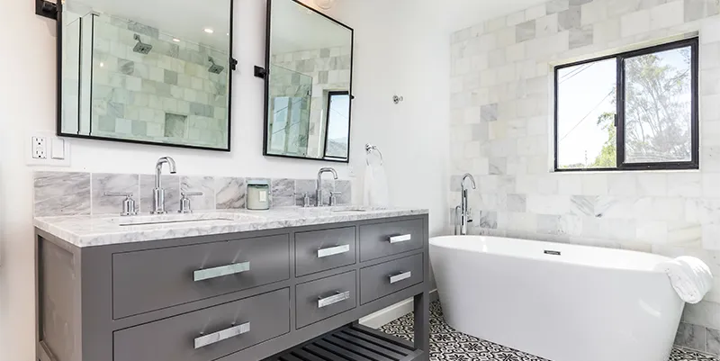 Modern primary bathroom renovation showcasing a freestanding soaking tub, dark double vanity, and patterned tile floor by LK Home Renovations.