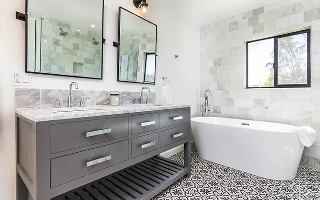 Modern primary bathroom renovation showcasing a freestanding soaking tub, dark double vanity, and patterned tile floor by LK Home Renovations.