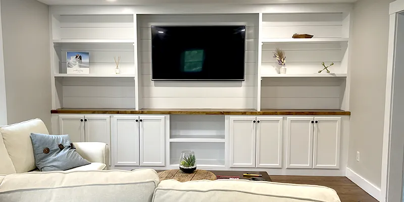 Custom built-in white bookshelves and cabinets surrounding a modern fireplace in a Massachusetts living room.